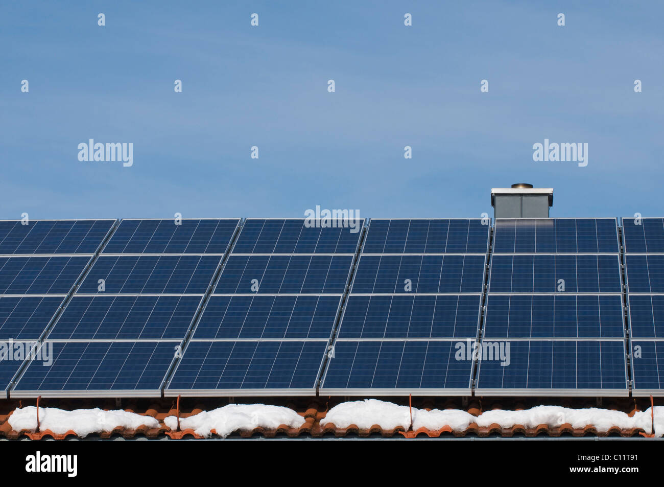 Sonnenkollektoren auf dem Dach eines Hauses mit Schneeflecken, erneuerbare Energien Stockfoto
