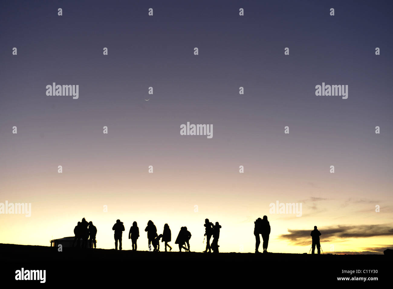 Silhouette von Menschen und Fotografen auf Berg in der Morgendämmerung. Silhouetten von Menschen gegen den Nachthimmel. Nach einem Rückgang. Stockfoto