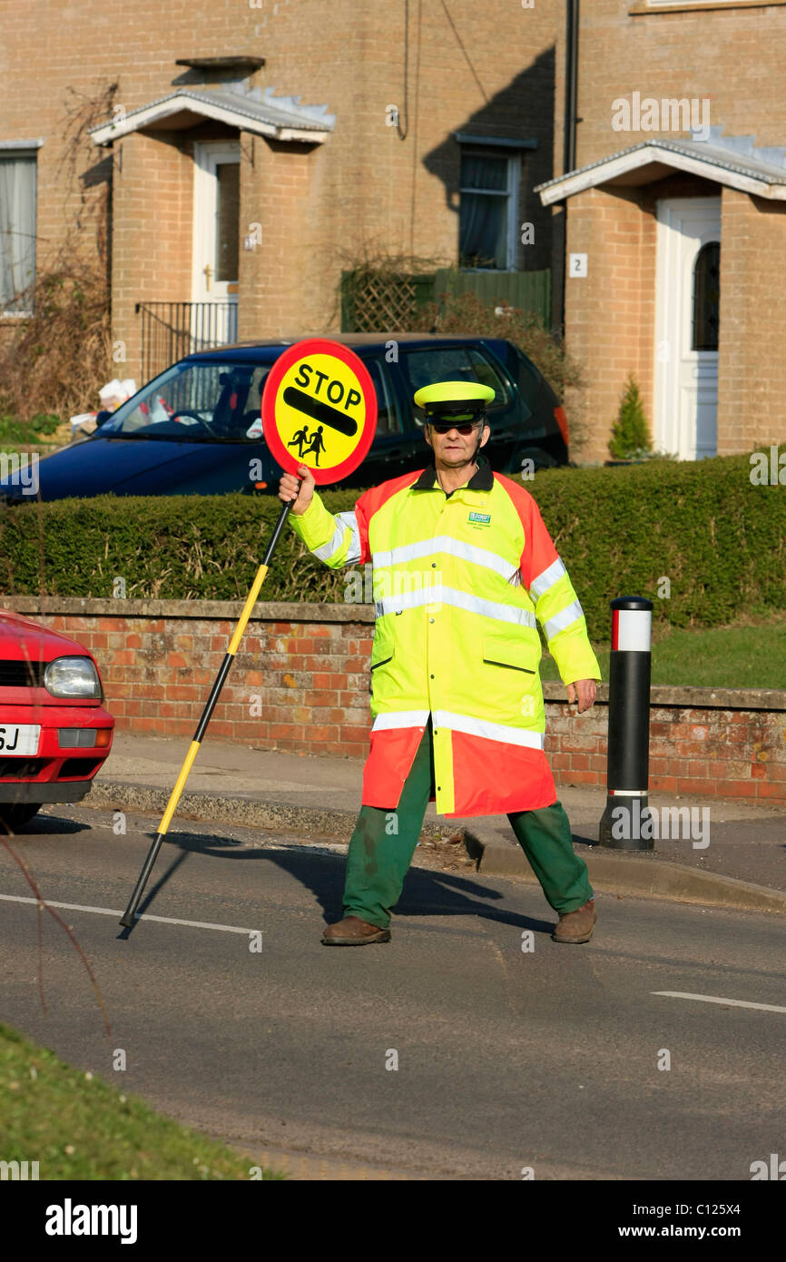 Ein Lollipop-Mann tut seine Pflicht, die Schülerinnen und Schüler über eine stark befahrene Straße zu sehen Stockfoto