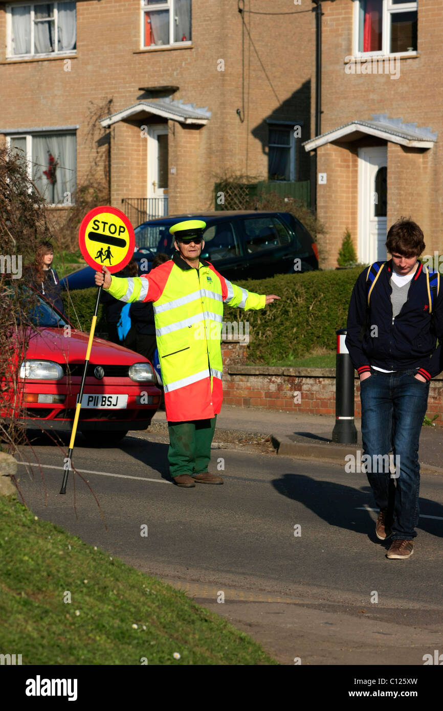 Ein Lollipop-Mann tut seine Pflicht, die Schülerinnen und Schüler über eine stark befahrene Straße zu sehen Stockfoto