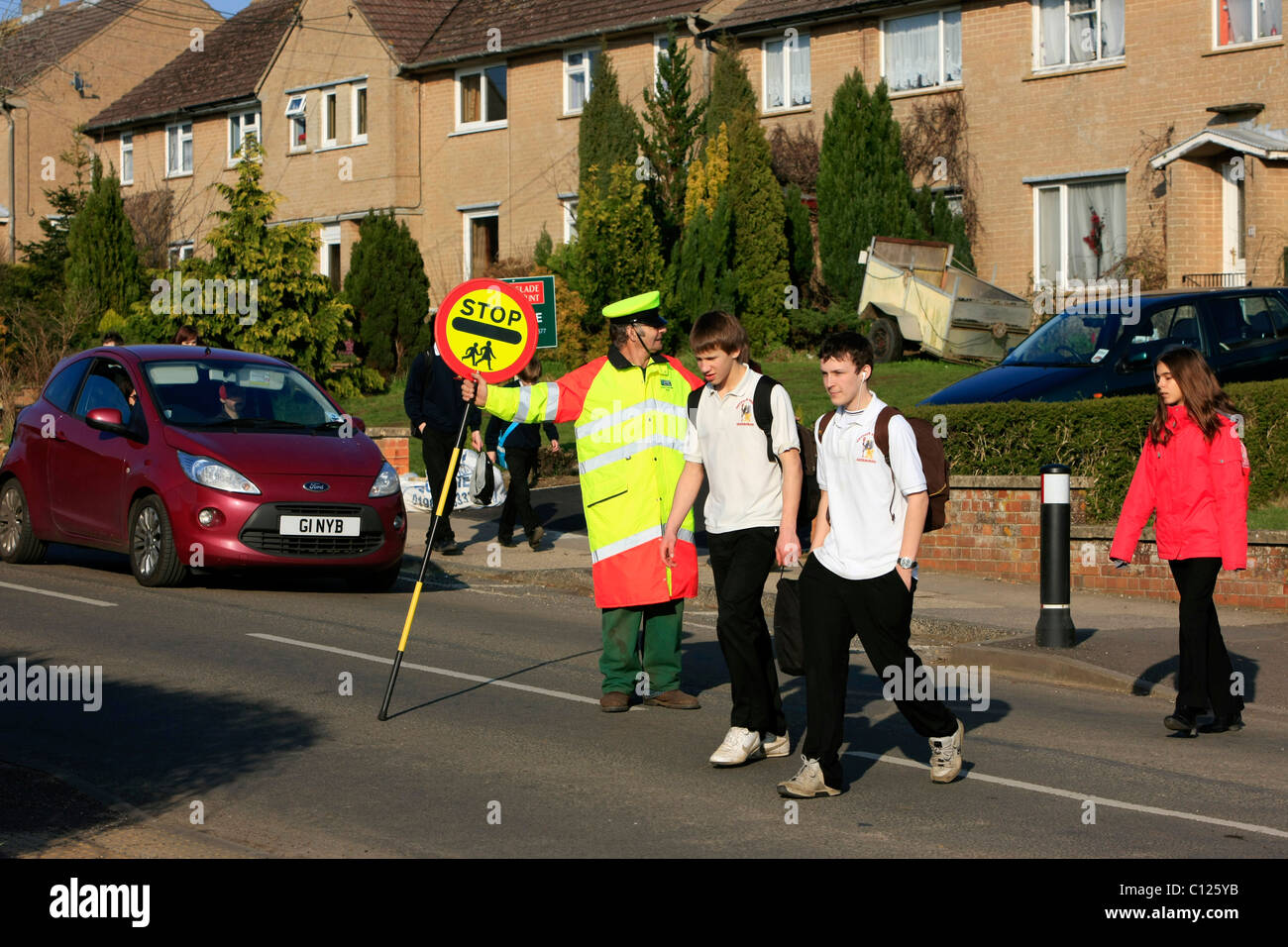 Ein Lollipop-Mann tut seine Pflicht, die Schülerinnen und Schüler über eine stark befahrene Straße zu sehen Stockfoto