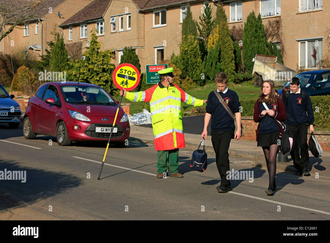 Ein Lollipop-Mann tut seine Pflicht, die Schülerinnen und Schüler über eine stark befahrene Straße zu sehen Stockfoto