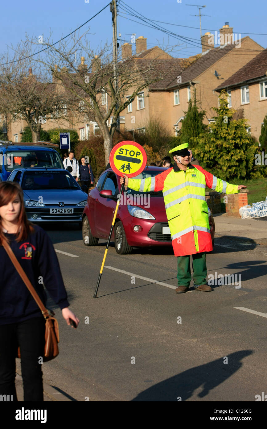 Ein Lollipop-Mann tut seine Pflicht, die Schülerinnen und Schüler über eine stark befahrene Straße zu sehen Stockfoto