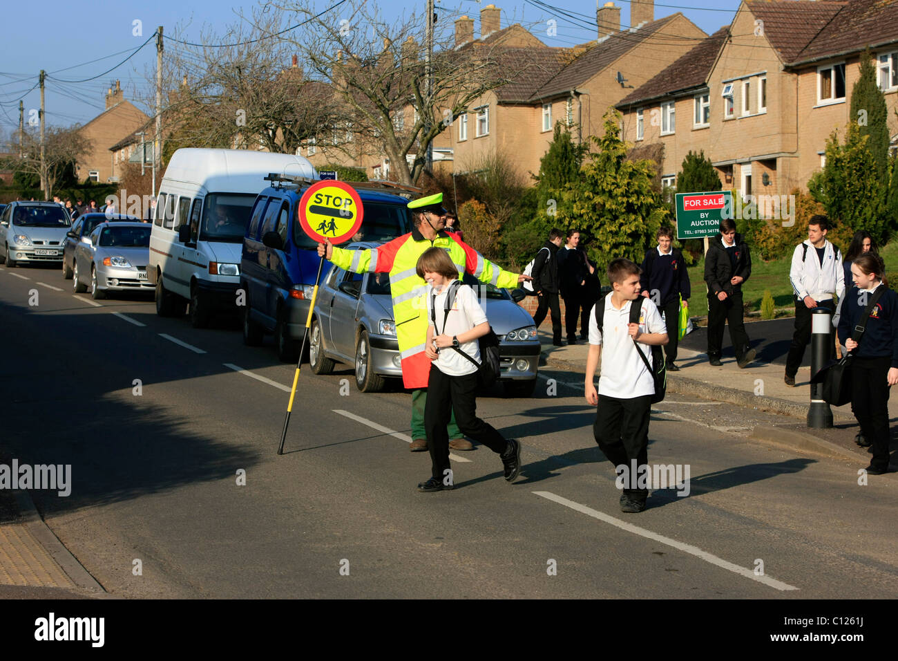 Ein Lollipop-Mann tut seine Pflicht, die Schülerinnen und Schüler über eine stark befahrene Straße zu sehen Stockfoto