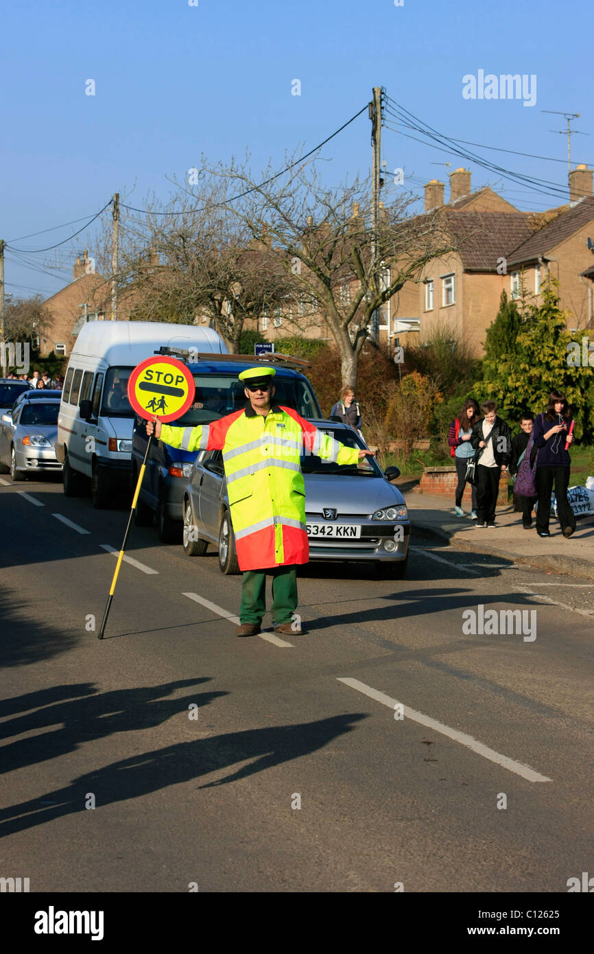 Ein Lollipop-Mann tut seine Pflicht, die Schülerinnen und Schüler über eine stark befahrene Straße zu sehen Stockfoto