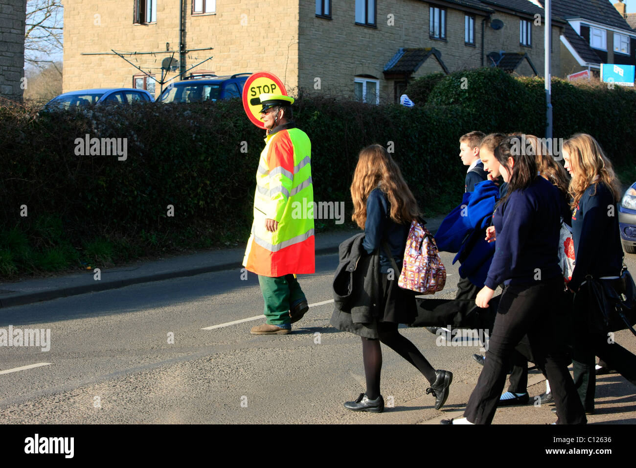 Ein Lollipop-Mann tut seine Pflicht, die Schülerinnen und Schüler über eine stark befahrene Straße zu sehen Stockfoto