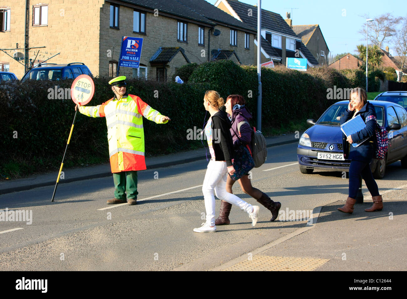 Ein Lollipop-Mann tut seine Pflicht, die Schülerinnen und Schüler über eine stark befahrene Straße zu sehen Stockfoto