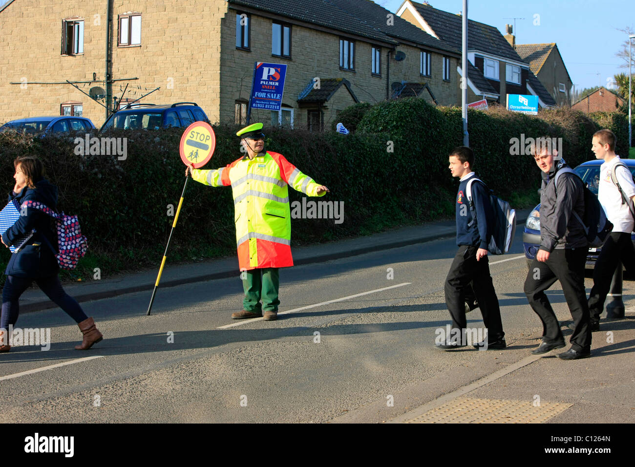 Ein Lollipop-Mann tut seine Pflicht, die Schülerinnen und Schüler über eine stark befahrene Straße zu sehen Stockfoto