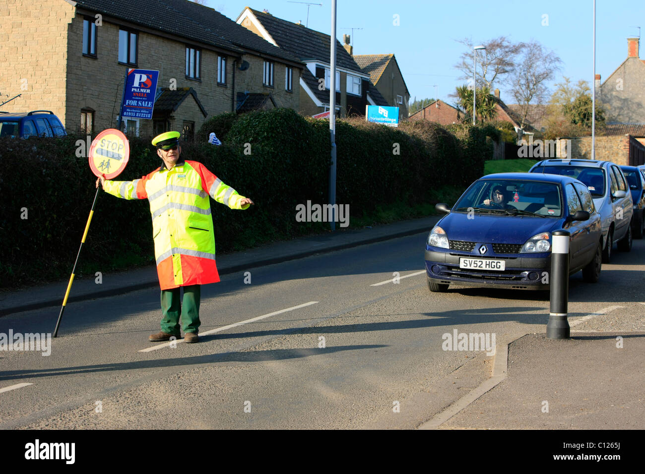 Ein Lollipop-Mann tut seine Pflicht, die Schülerinnen und Schüler über eine stark befahrene Straße zu sehen Stockfoto