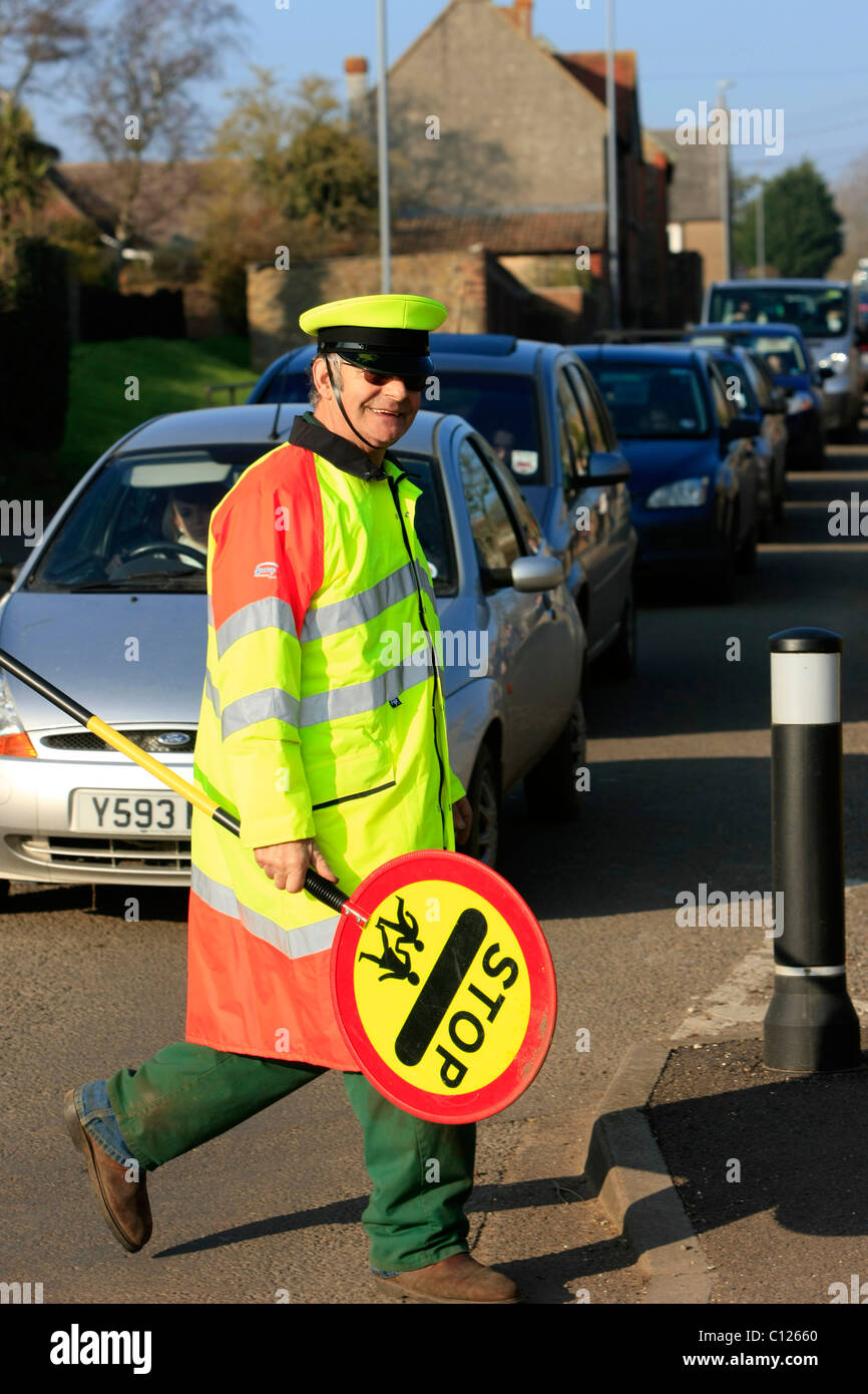 Ein Lollipop-Mann tut seine Pflicht, die Schülerinnen und Schüler über eine stark befahrene Straße zu sehen Stockfoto