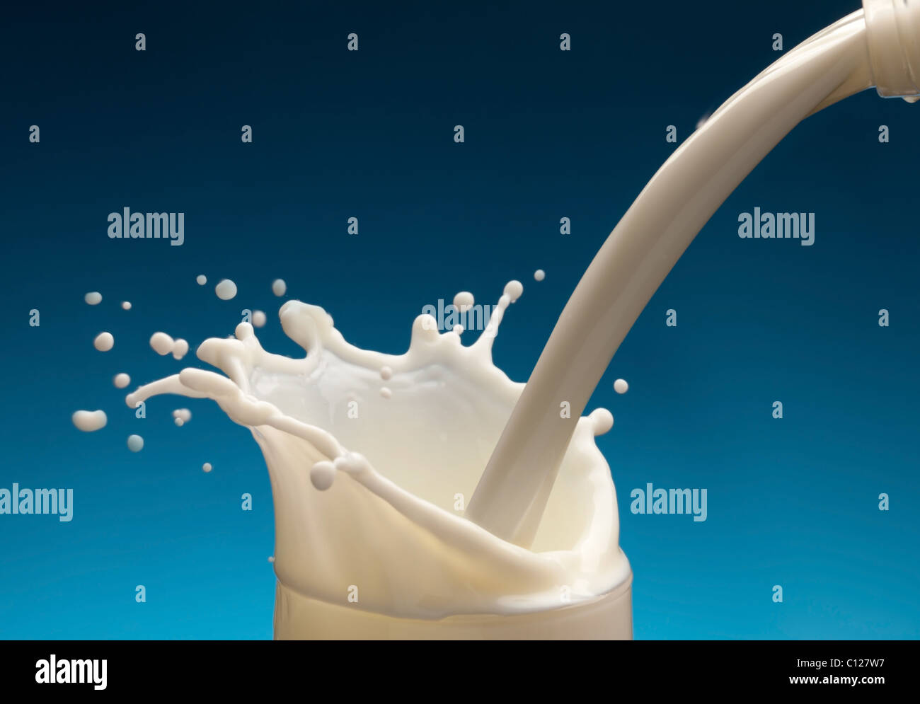 Spritzer Milch aus dem Glas auf blauem Hintergrund Stockfoto