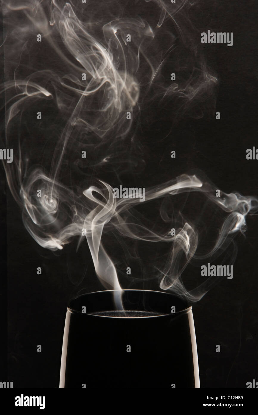 Weißer Rauch steigt aus einer schwarzen Kerze vor einem schwarzen Hintergrund. Stockfoto