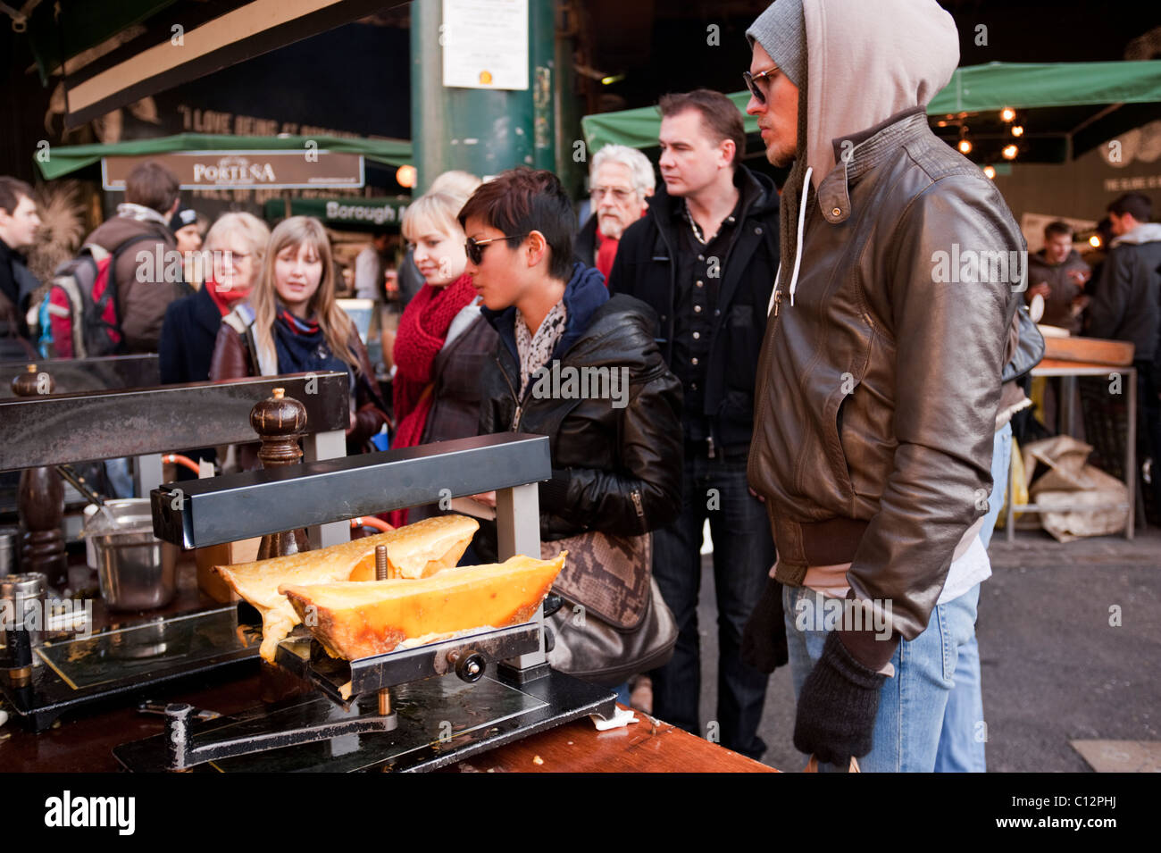 Raclette Käse grillen- und eine Schlange von Kunden - ein beliebtes Nahrungsmittel stall am Londoner Borough Market. Stockfoto