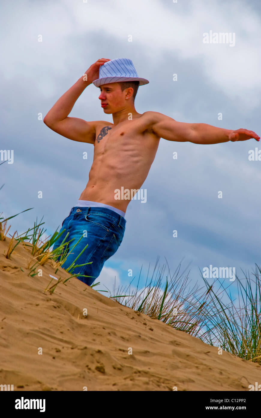 Drilliche junger Mann steht mit der Hand auf Kopf auf einer Sanddüne Stockfoto
