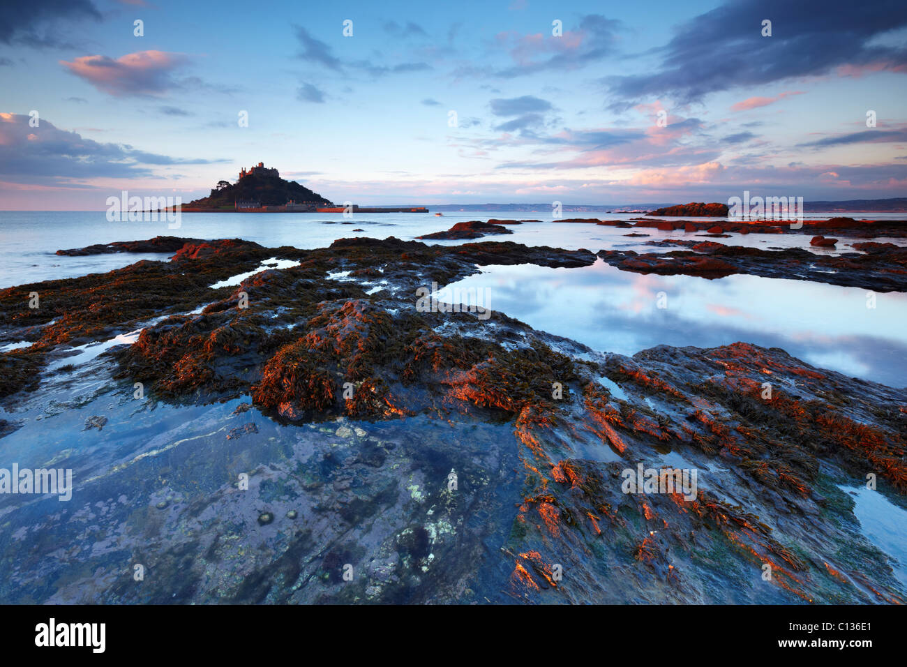 St. Michaels Mount im Schein der Morgensonne beleuchtet. Die zurückweichenden Flut schafft Fels-Pools, die den Sonnenaufgang Himmel widerspiegeln. Stockfoto