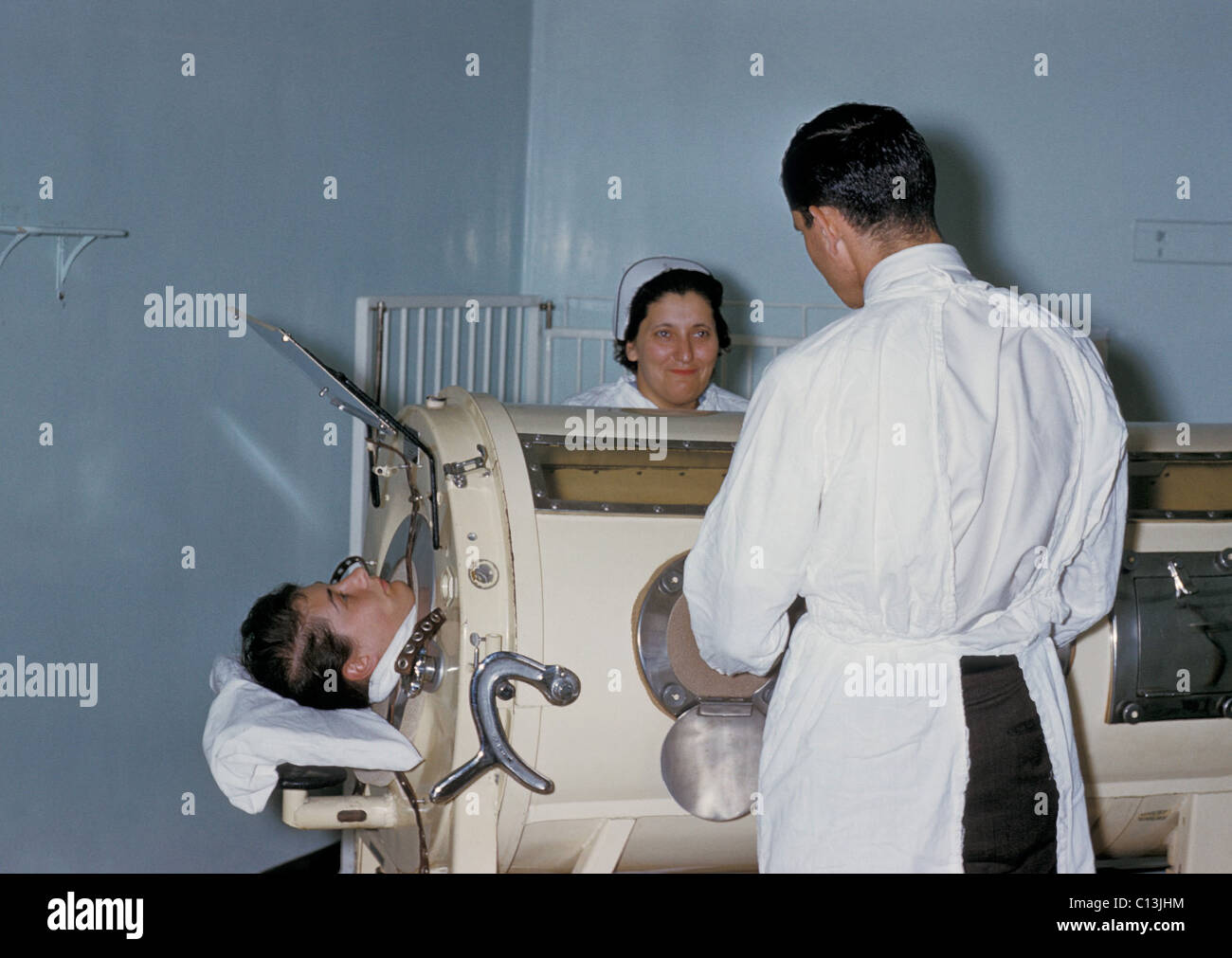 Krankenhauspersonal untersuchen ein Patienten im Respirator Tank, eiserne Lunge, während einer Polio-Epidemie in Rhode Island. Die eiserne Lunge umhüllt die Brusthöhle extern in einer luftdichten Kammer. Die Kammer wurde verwendet, um einen Unterdruck in der Brusthöhle, wodurch Luft in die Lungen zu Hämoglobin Druckausgleich hetzen zu erstellen. Ca. 1960. Stockfoto