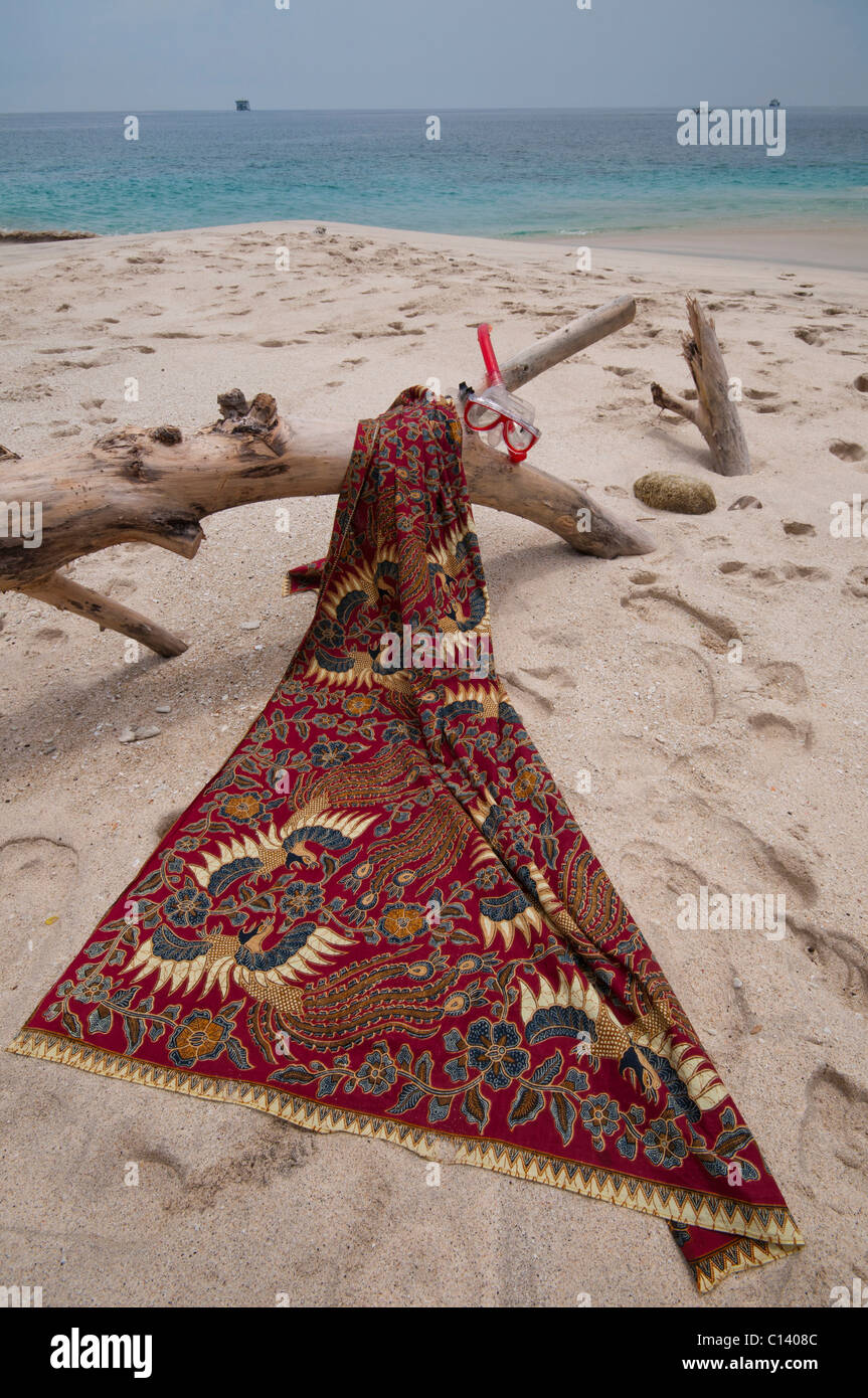 Eine Batik-Sarong drapiert über Treibholz auf dem weißen Sand Strand von Bias Tegal in Padang Bai auf Bali Stockfoto