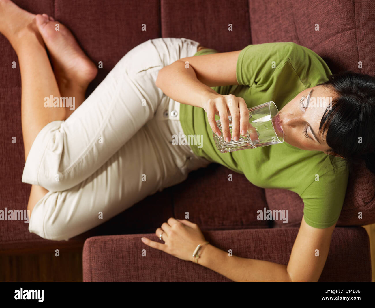 Entspannen Sie sich auf Sofa mit Glas Wasser Erwachsene Frau Mitte. Erhöhte Ansicht, horizontale Form, Tiefenschärfe, in voller Länge Stockfoto