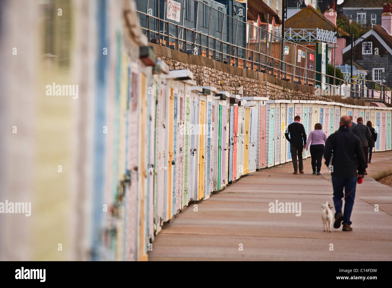 Am frühen Morgen Wanderer entlang der Promenade in Lyme Regis in Dorset. Neben ihnen sind Reihen von bunten Strandhäuschen. Stockfoto