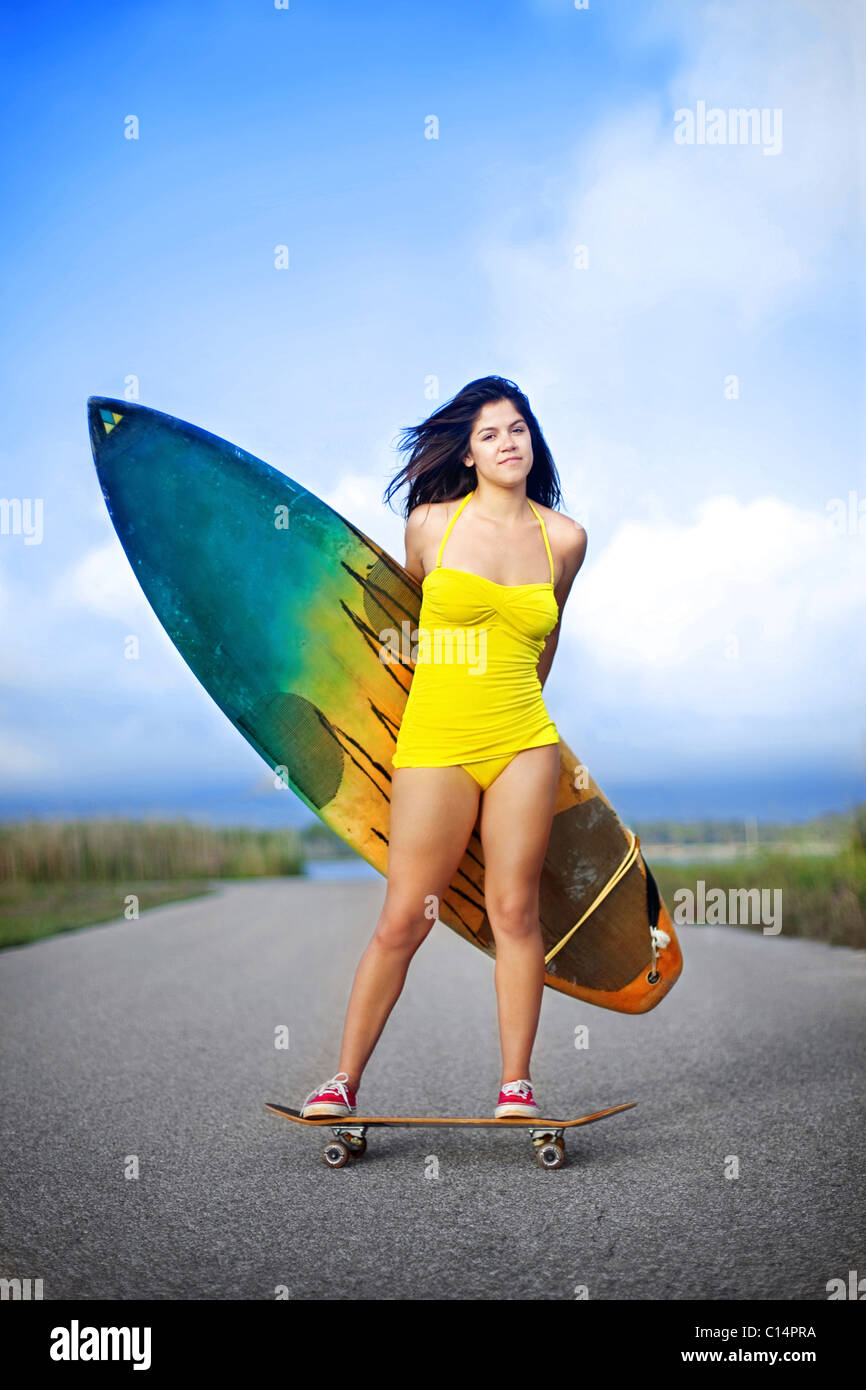 junge Frau trägt gelbe Badeanzug auf Skateboard auf der Straße stehen und  halten Surfbrett Stockfotografie - Alamy