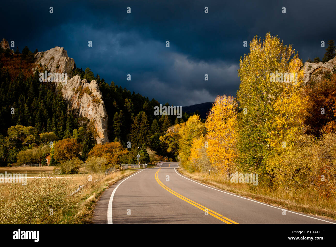 Autobahn mit Bäumen in Herbstfarben und stürmischen Himmel.  Walsenburg, Colorado. Stockfoto
