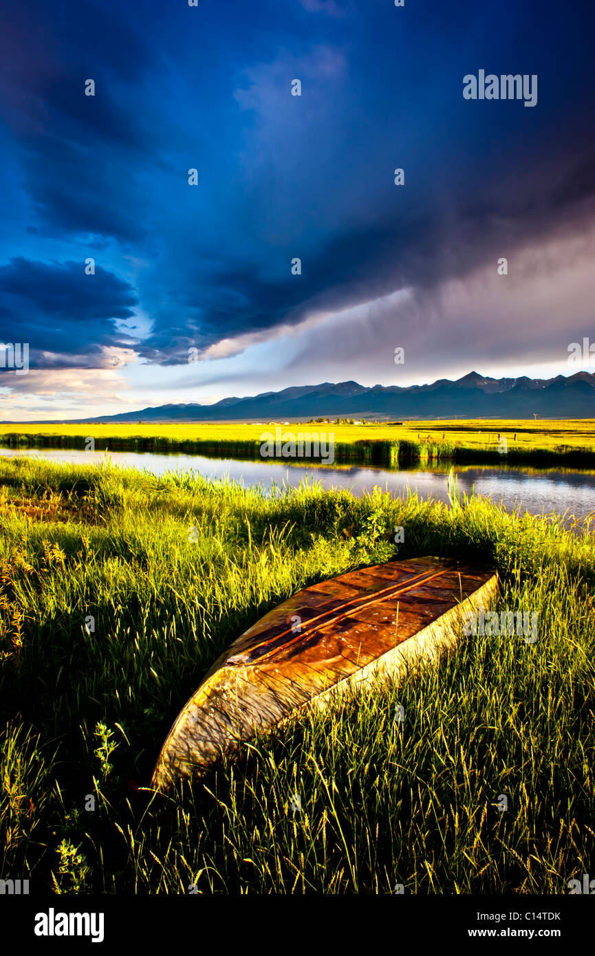 Boot in Grasgrün mit Teich, Bergen und stürmischen Himmel.  Westcliffe, Colorado. Stockfoto