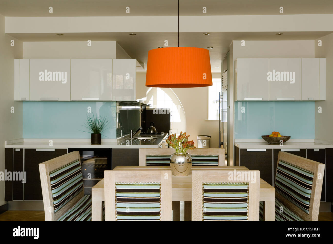 Große orange Lampenschirm über dem Esstisch in offene Küche mit gestreiften Stühle Stockfoto