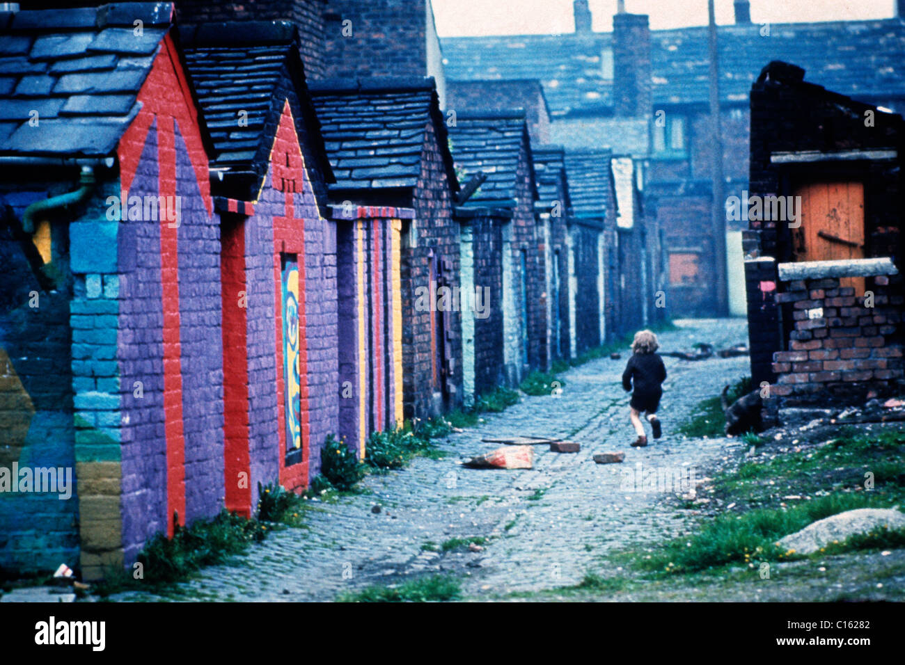 Ein Junge Kind Rückansicht hinter spielen heruntergelaufen Eine Gasse mit bunten Wandmalereien in der hinteren Gasse 1970s Lancashire Nord-England Großbritannien 1975 KATHY DEWITT Stockfoto