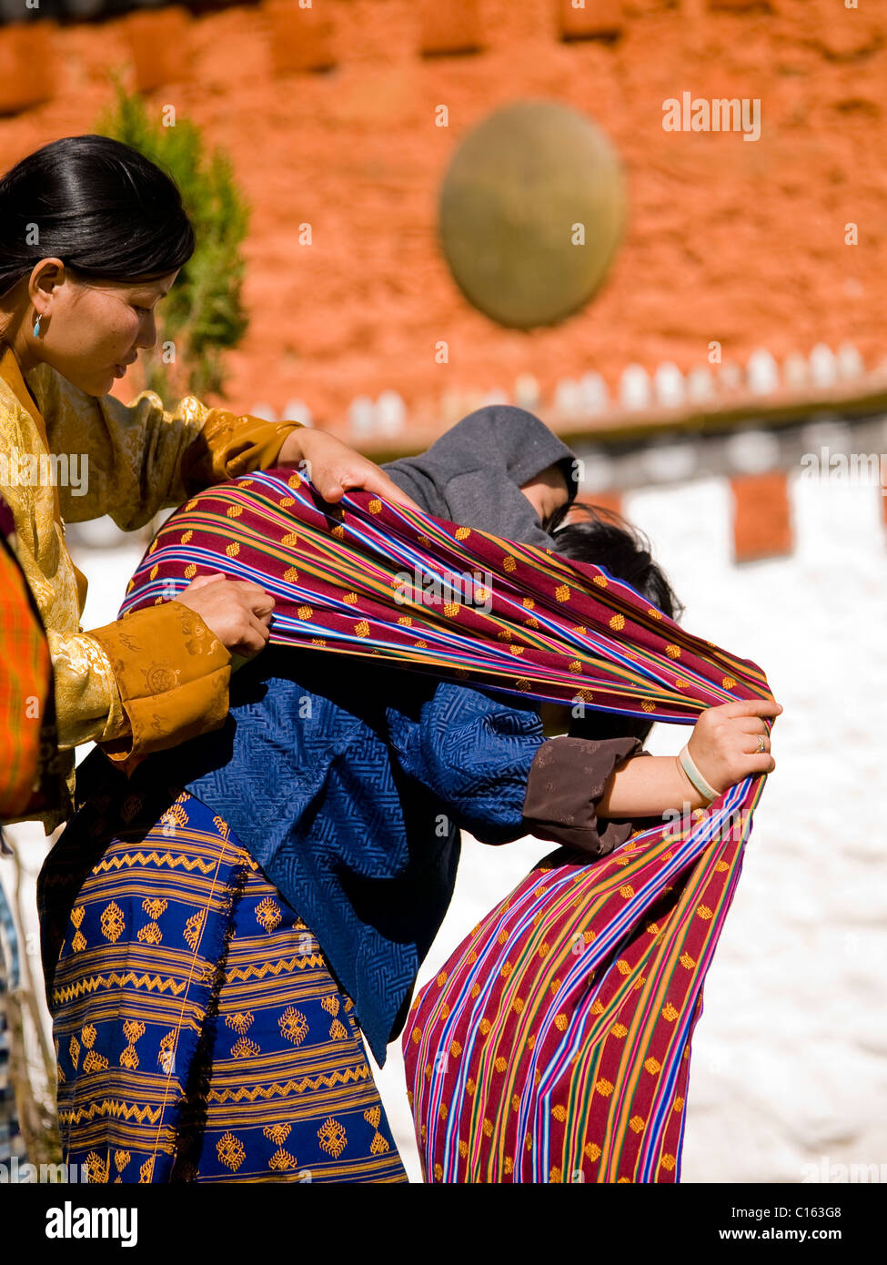 junge Frau trägt ein traditionelles Kira hilft eine andere Frau mit ihrem Baby auf dem Rücken binden Stockfoto