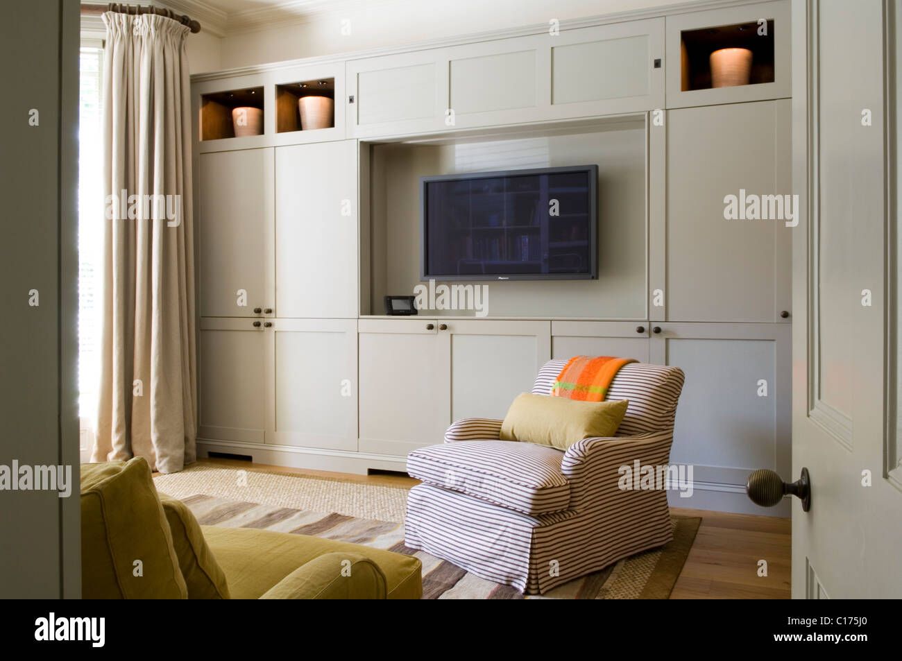 Flachbild-TV im Wohnzimmer mit Einbauschränken und Sessel Stockfoto