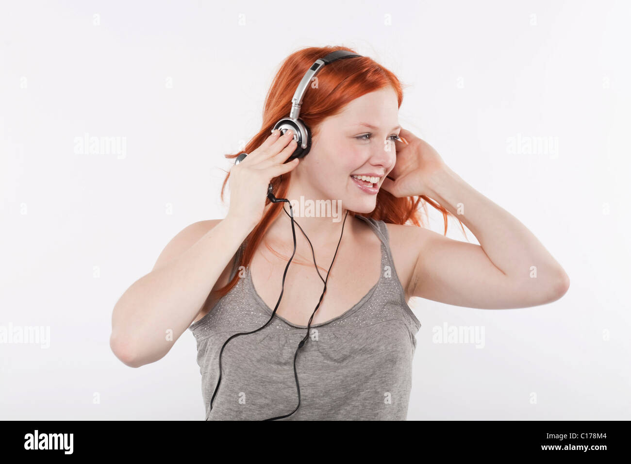 Junge Frau mit langen roten Haaren, die Musik über Kopfhörer hören Stockfoto