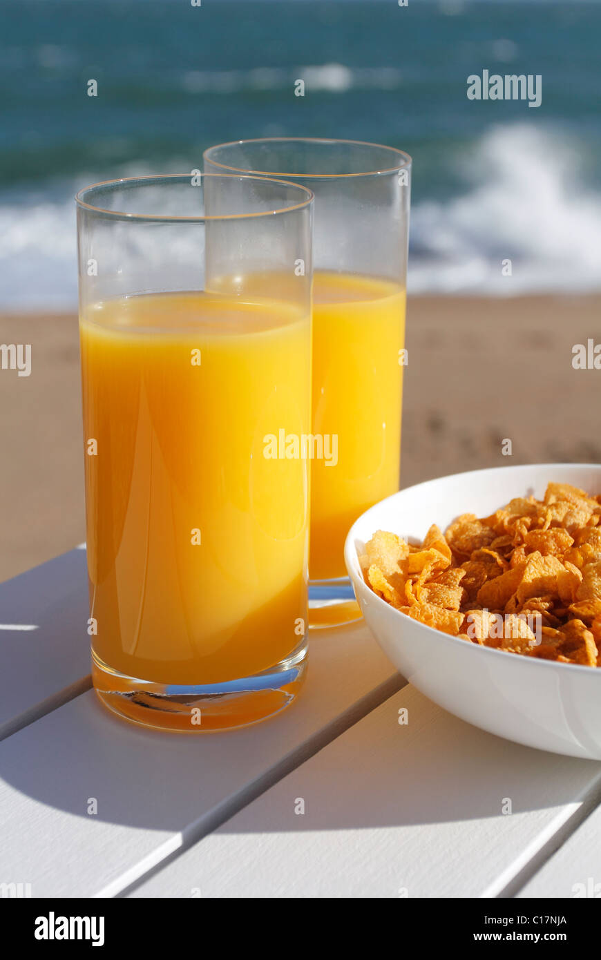 Gläser Orangensaft und eine Schüssel Müsli am Meer. Stockfoto