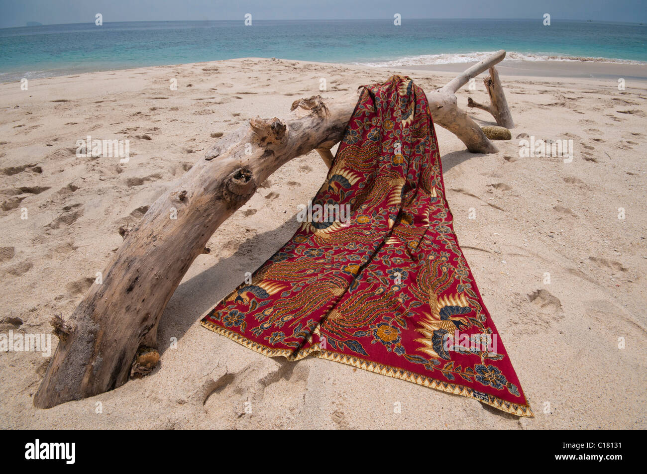 Eine Batik-Sarong drapiert über ein Treibholz-Protokoll auf dem weißen Sand Strand von Bias Tegal in Padang Bai, Bali Stockfoto