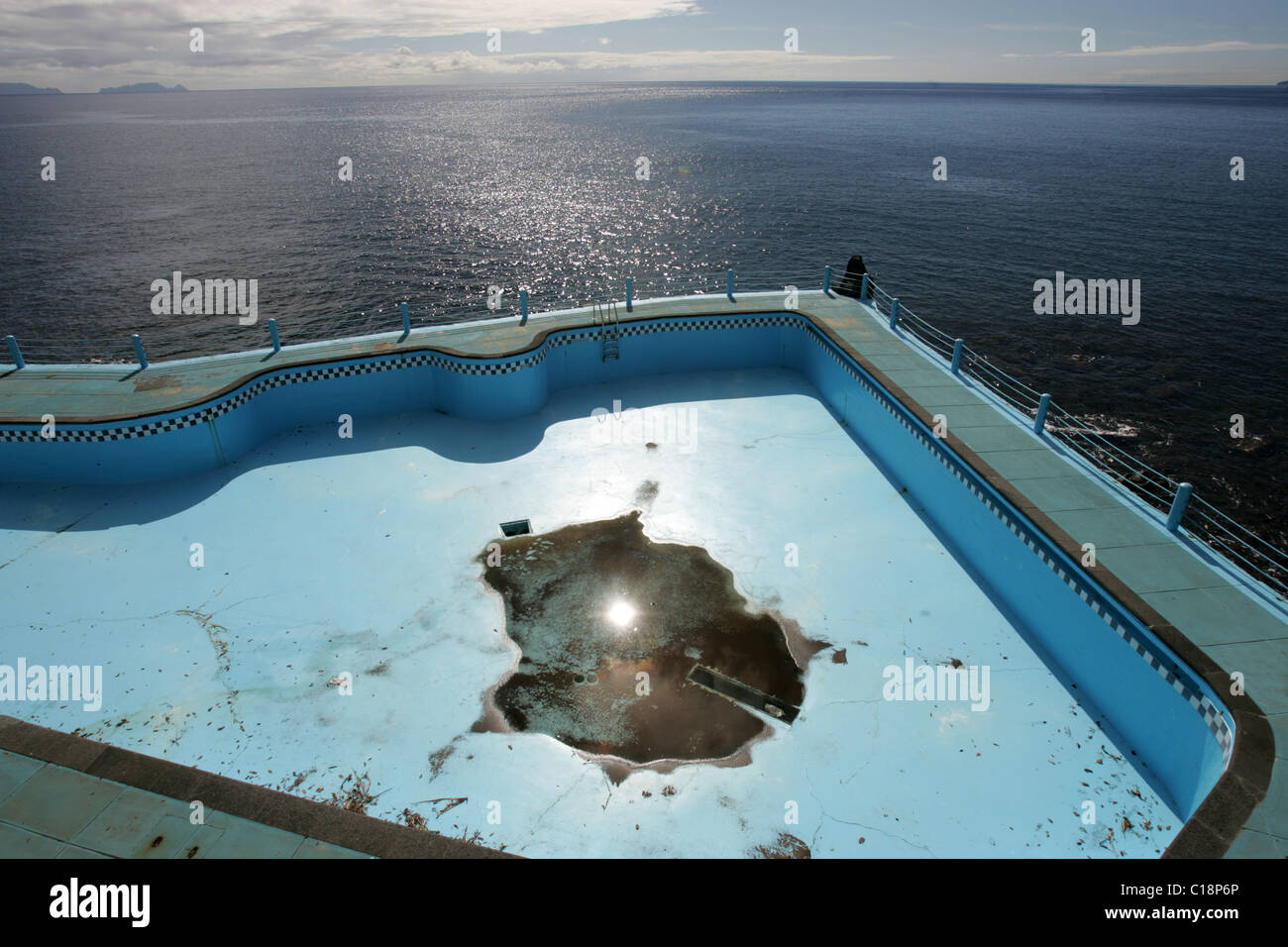 Leere Schwimmbecken mit kleinen Pfütze neben Meer. Stockfoto