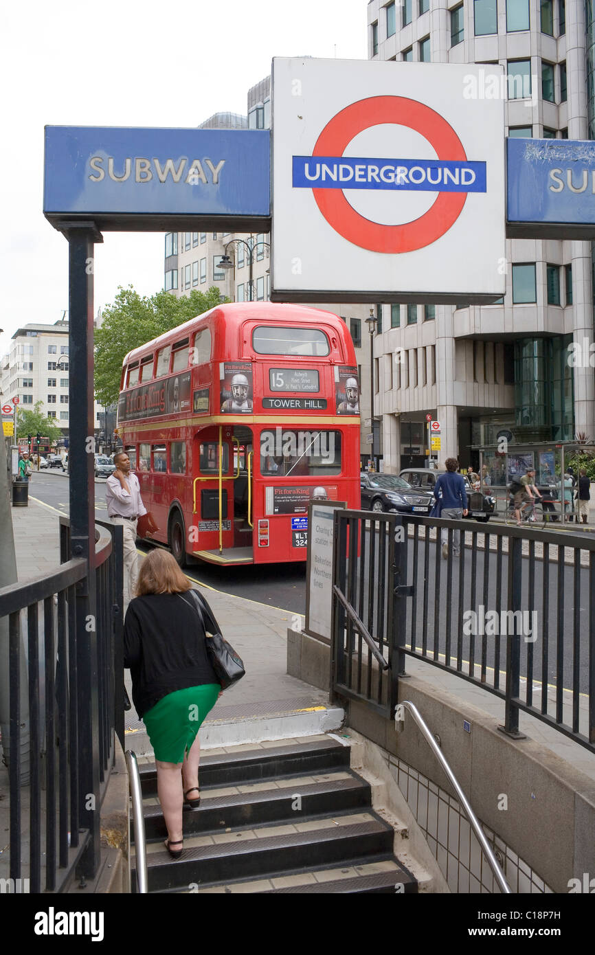 Eine Frau in einem grünen Rock verlässt eine Londoner U-Bahn u-Bahnstation als eine rote Routemaster Nummer 15 Bus Drices Vergangenheit. Stockfoto