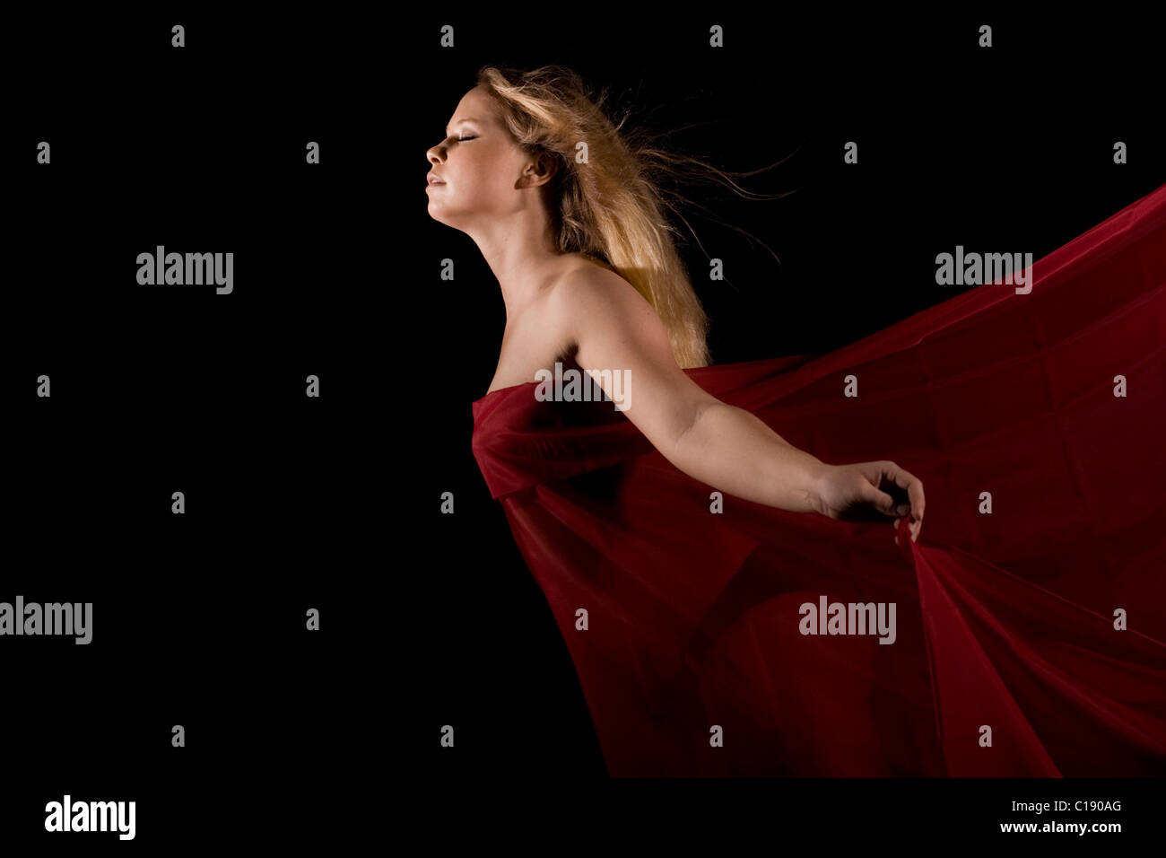 Junge blonde Frau in rotes Tuch vor schwarzem Hintergrund gewickelt Stockfoto