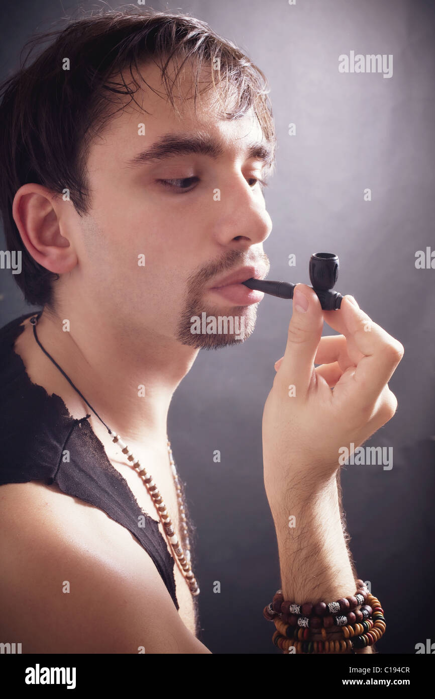 junger Mann raucht kleine Pfeife auf schwarzem Hintergrund Stockfoto