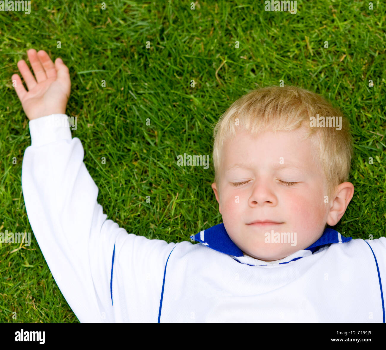 4-jähriger Junge mit einem Fußballtrikot in der Wiese liegend Stockfoto