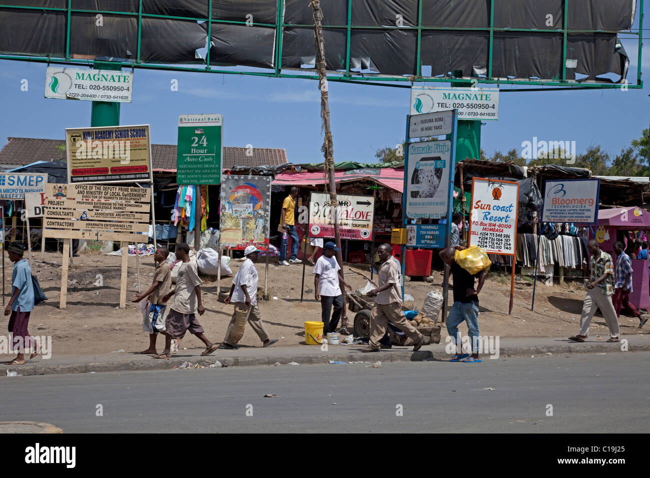 Afrikaner, die vorbei an Werbung Bill Bretter Werbetafeln in lässigen Straßenszene Mombasa Kenia Stockfoto