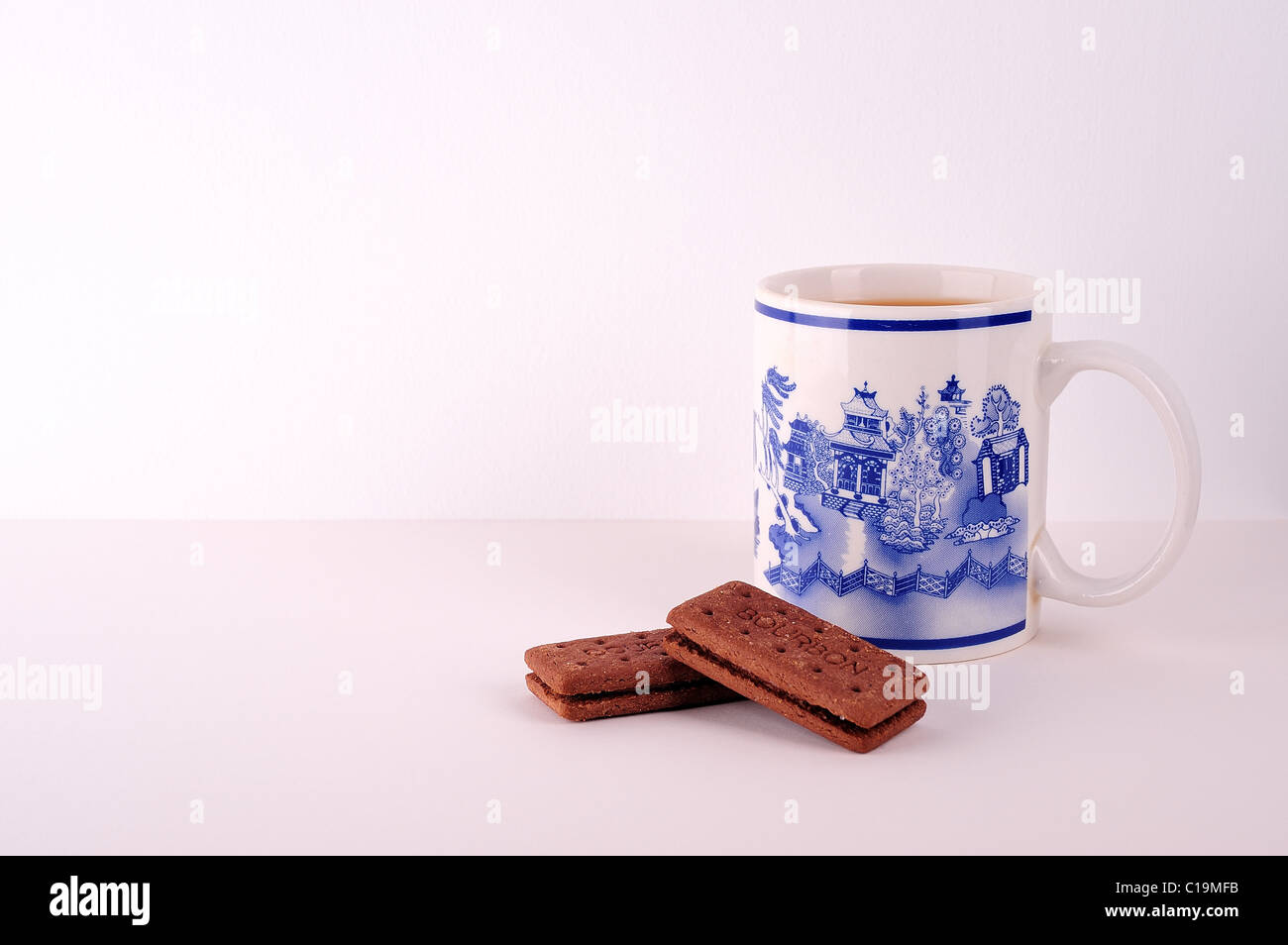 Eine Tasse Tee und zwei Bourbon Gebäck, der Becher ist Willow Muster, und sie sind mit einem weißen Hintergrund. Stockfoto