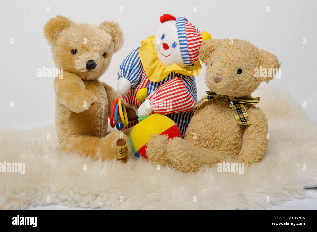 Zwei traditionelle Teddybären und ein buntes Spielzeug-Clown sitzend auf einem Schaffell-Teppich. Eine nette Feier Bild für ein neues Baby. Stockfoto