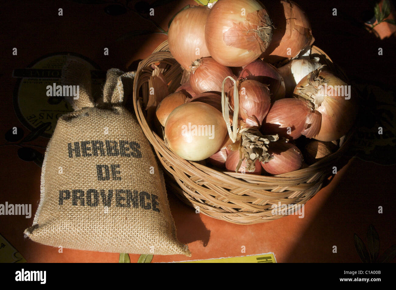 Gelbe Zwiebeln und Schalotten in einem Weidenkorb mit Kräutern der Provence im Sommerlicht einer Küche in der Provence Stockfoto