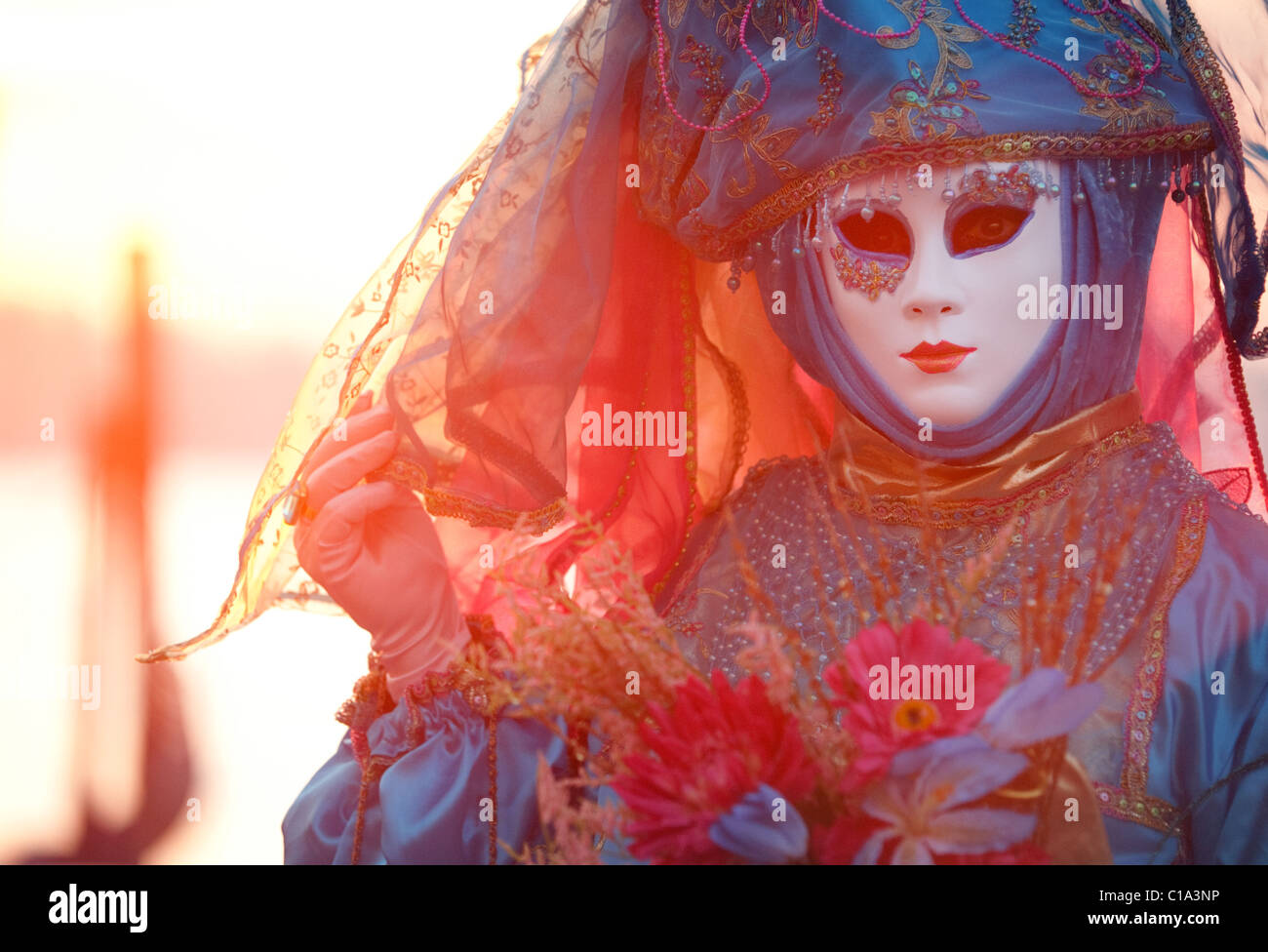 Ein Modell in Maske und Kostüm mit dem Sonnenaufgang hinter ihr, der Karneval von Venedig, Venedig, Italien Stockfoto