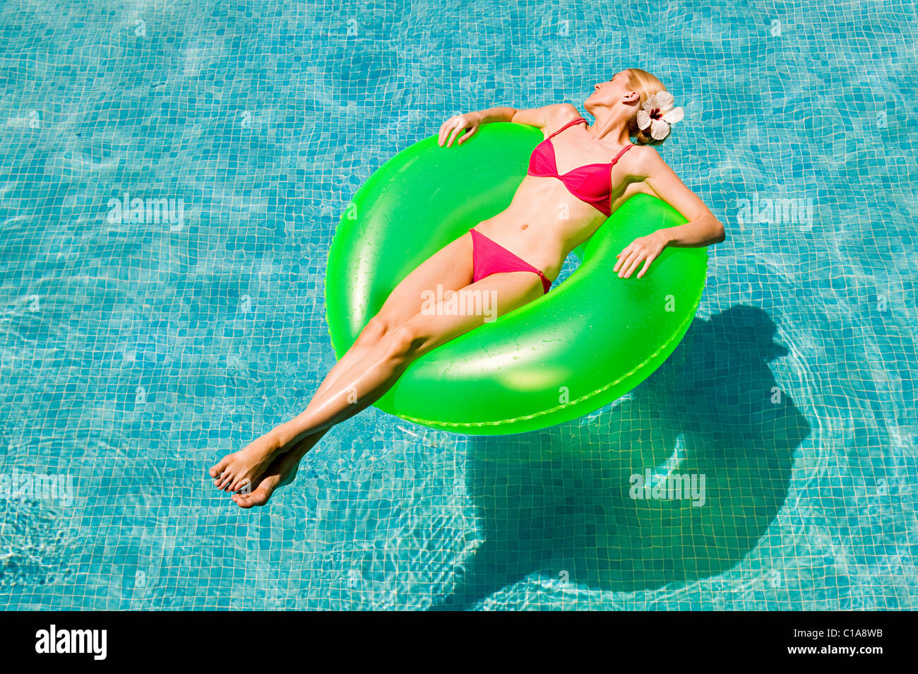 Junge Frau, die auf grünen aufblasbaren Ring im Schwimmbad schwimmen Stockfoto