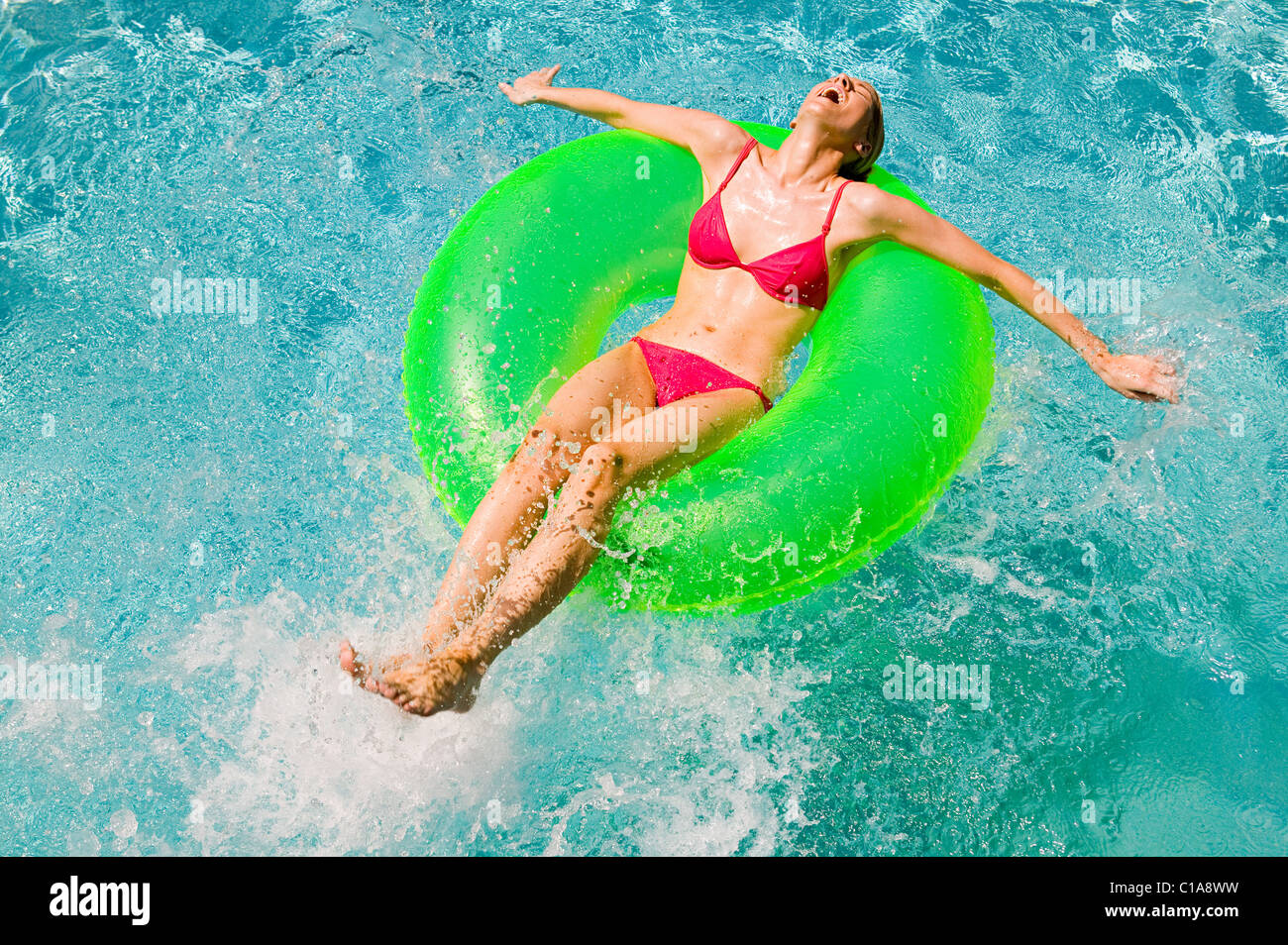 Junge Frau, die auf grünen aufblasbaren Ring im Schwimmbad schwimmen Stockfoto