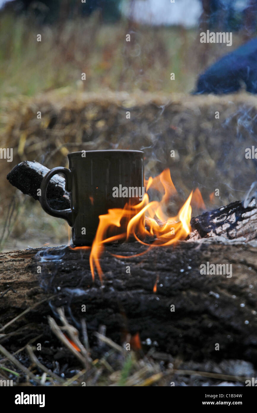 Eine Tasse Tee oder Kaffee aufwärmen über dem offenen Feuer während im Camp. Stockfoto
