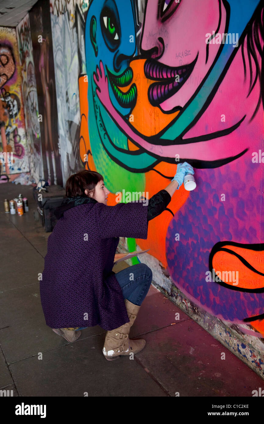 Weiblichen Graffiti Künstler Spritzlackierung eine Wand an der Southbank, London. Dieses Gebiet ist beliebt für Straßenkunst. Stockfoto