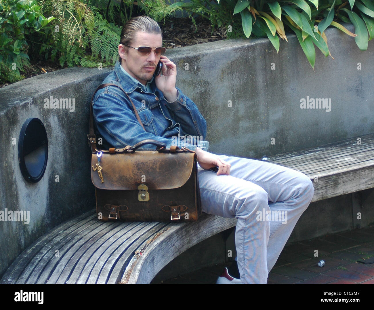 Ethan Hawke reden auf seinem Handy und trägt seine Ledertasche Tasche mit einem Star Wars C3PO Schlüssel Schlüsselanhänger Auckland City, Neuseeland Stockfoto