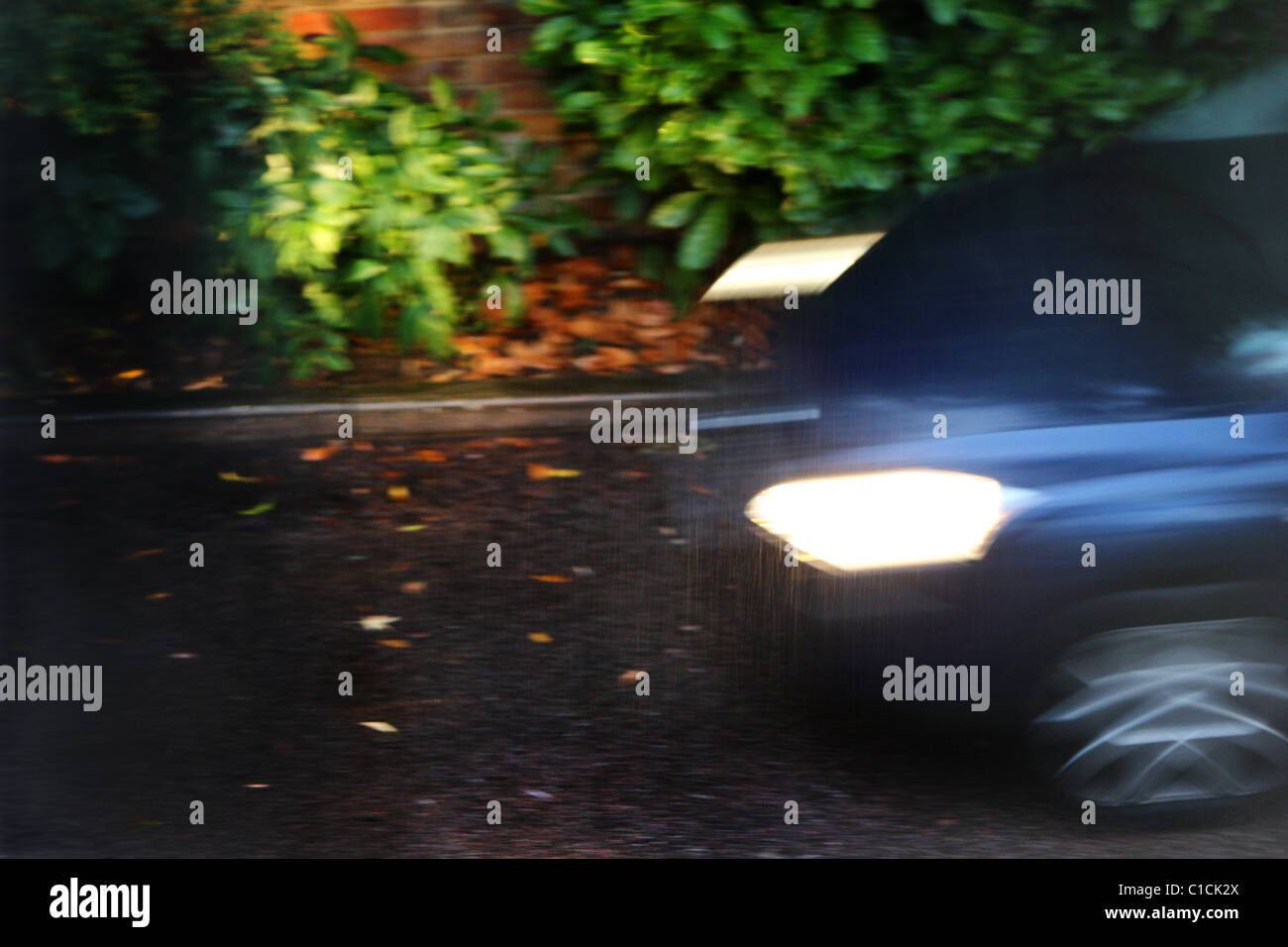 Bewegungsunschärfe eines Autos mit eingeschalteten Scheinwerfern in der Nacht, auf einer nassen Wohnstraße. Stockfoto