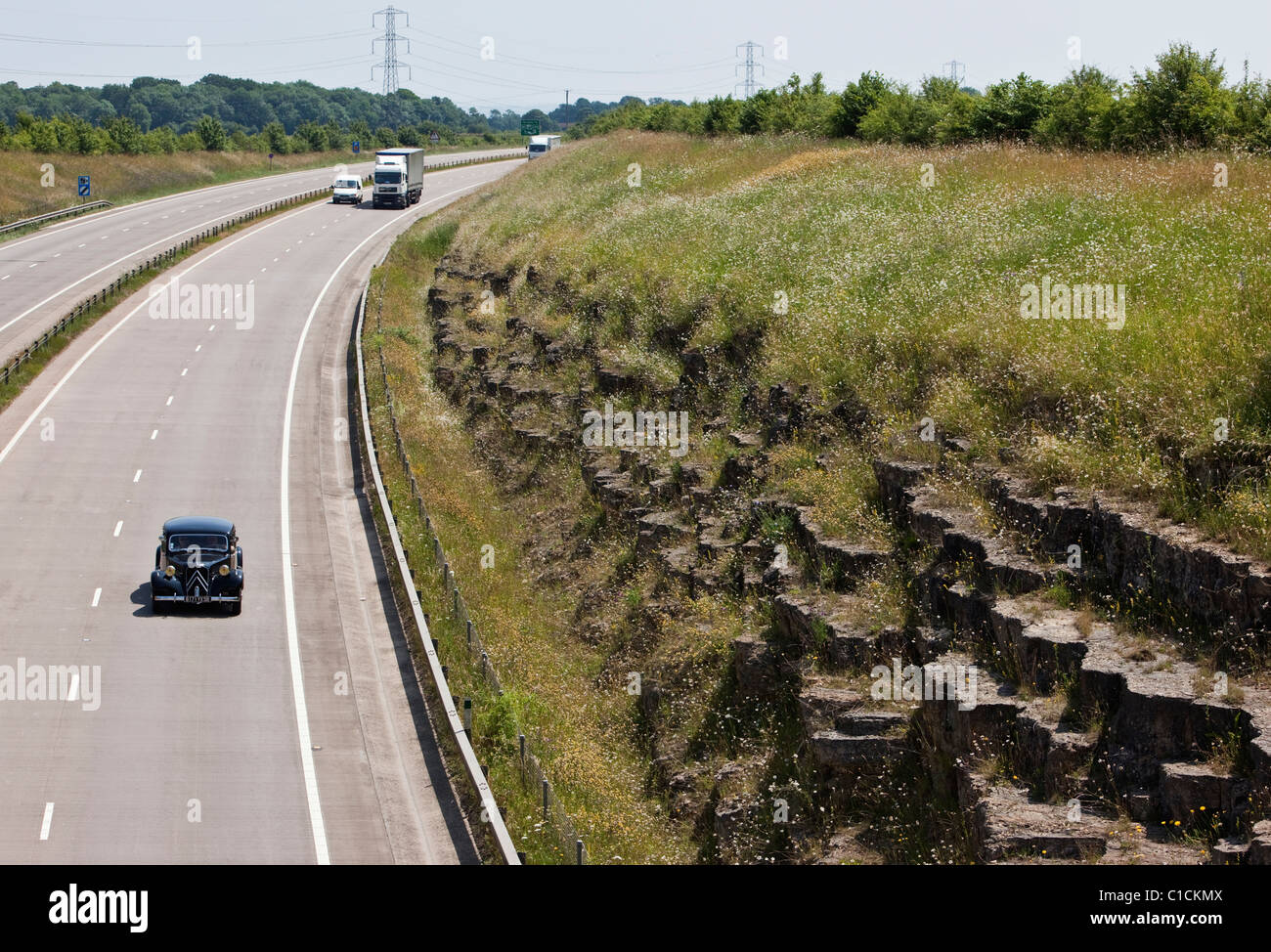 Ein Oldtimer Citroen und andere Verkehrsteilnehmer auf der zweispurigen A417 nördlich von Cirencester in den Cotswolds. Stockfoto